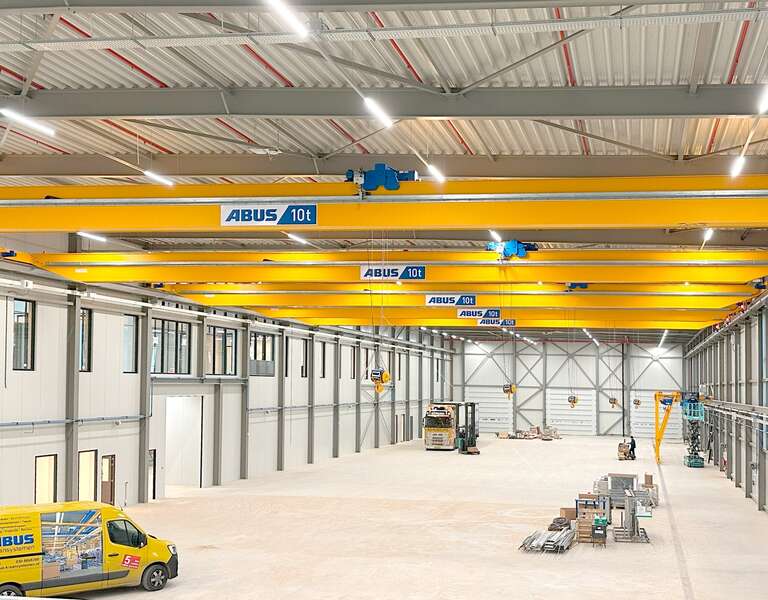 Eine Industriehalle mit mehreren Laufkranen auf einer Bahn Eine Industriehalle mit mehreren Laufkranen auf einer Bahn, im Vordergrund ein ABUS-Servicefahrzeug